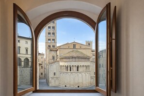 Une vue à travers une fenêtre en arc d’un bâtiment historique doté d’un clocher, d’une cour et d’une architecture environnante.