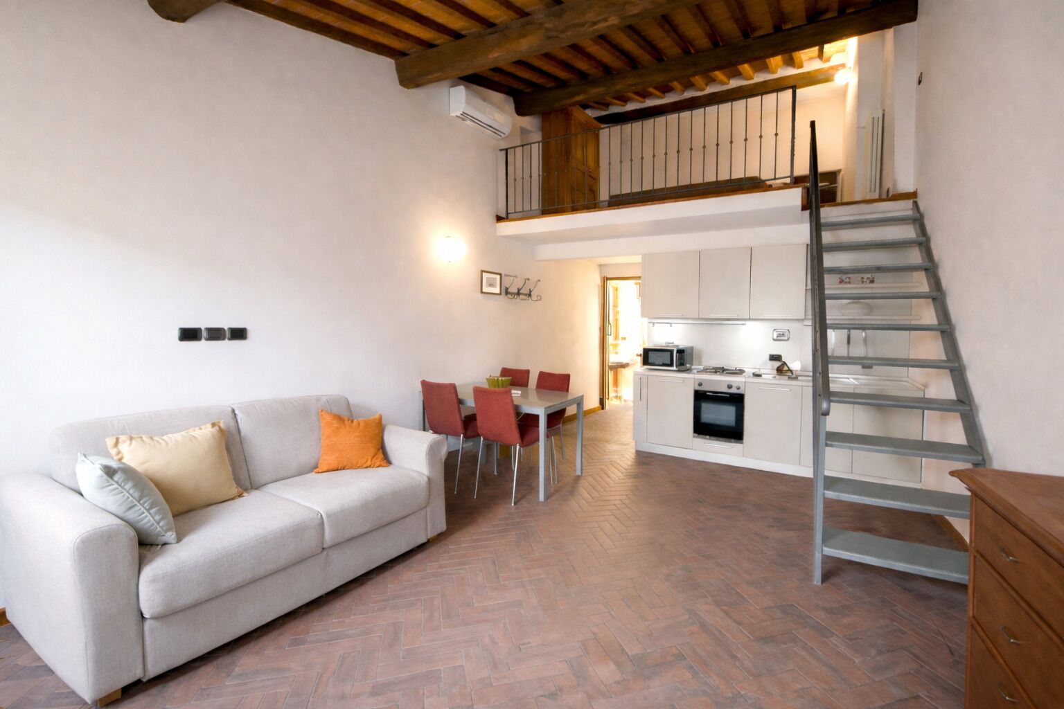 A spacious living area with a sofa, a dining table with chairs, a kitchen with a microwave, and a staircase.