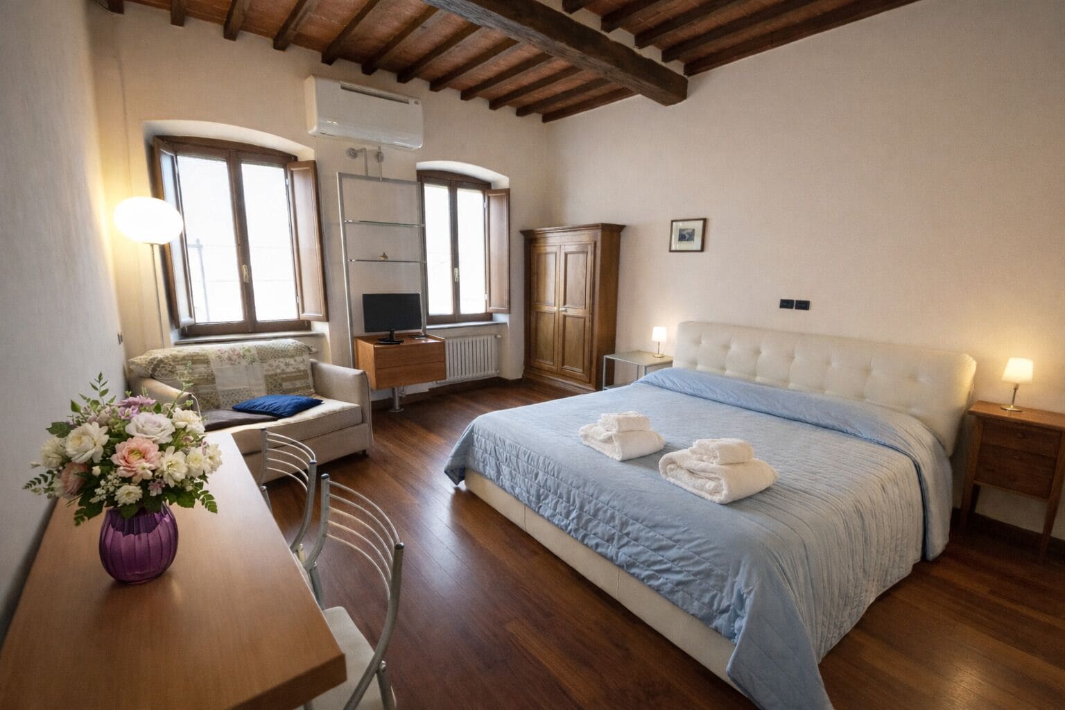 A bedroom with a bed, bedside tables, a desk, a chair, a dresser, and a radiator.