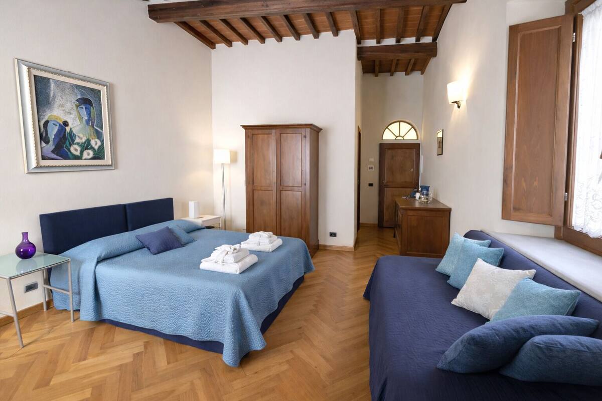 Un dormitorio con cama, sofá, suelo de madera, armario y un cuadro en la pared.