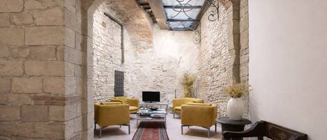 A cozy interior with stone walls, a vaulted ceiling, and a central seating area with yellow sofas and a coffee table.