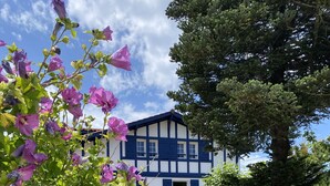 A two-story building with a white facade and blue trim, surrounded by a wooden fence and a stone pathway. - KALIKO (Bidart)