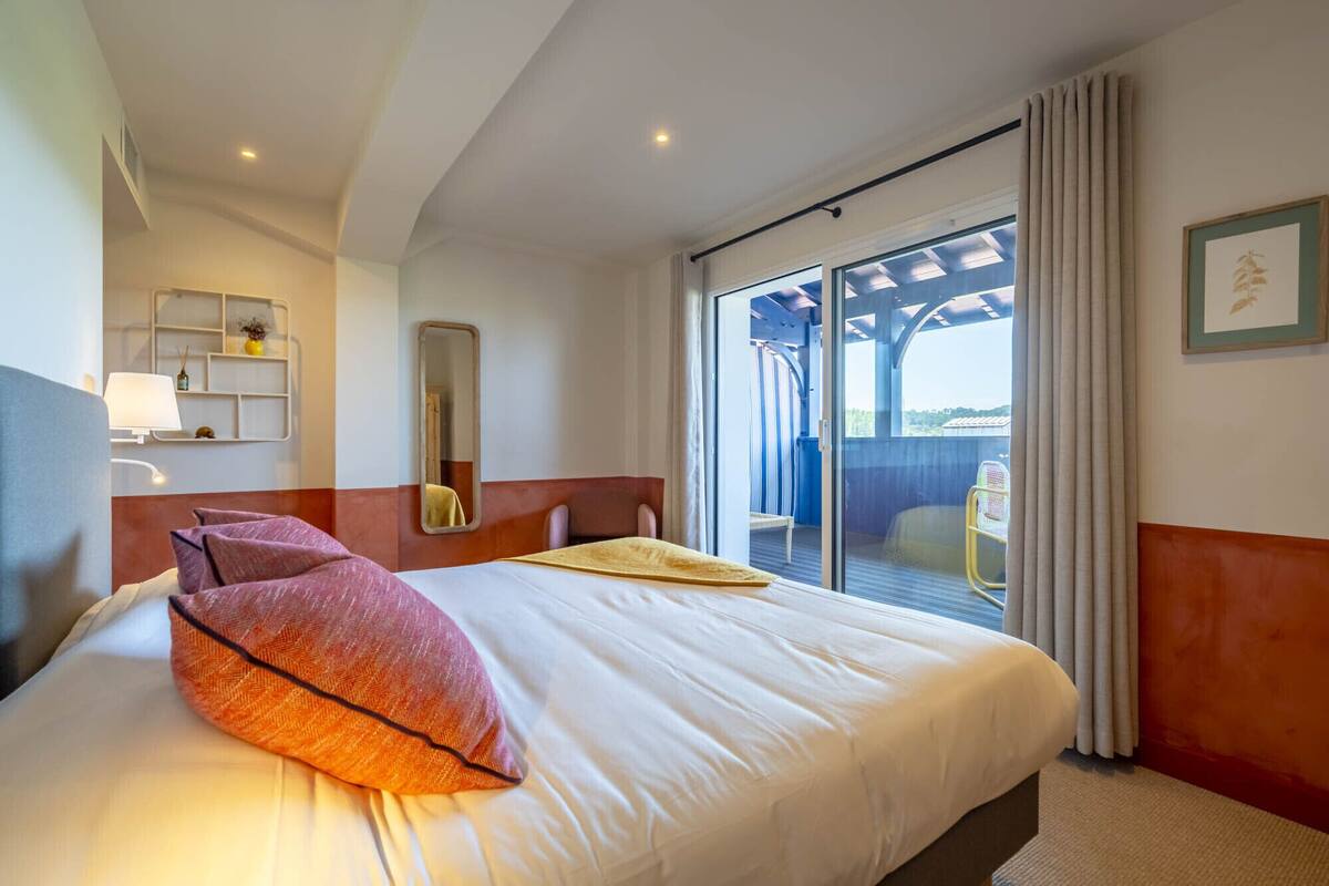 A hotel room with a bed, a large window, a balcony, and a view of the outdoors.