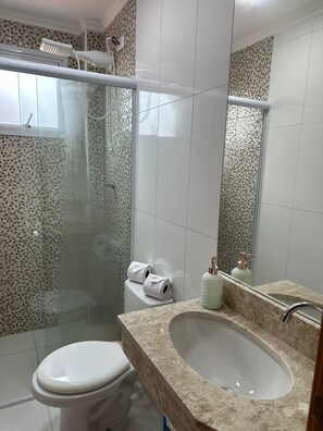 A bathroom with a glass-enclosed shower, a toilet, a sink with a marble countertop, and a mirror.