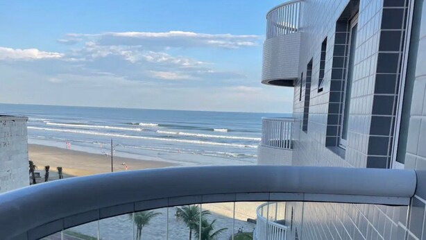 A modern building with a curved balcony overlooking a beach and street. - Maravilhoso Apto a Beira Mar (Praia Grande)