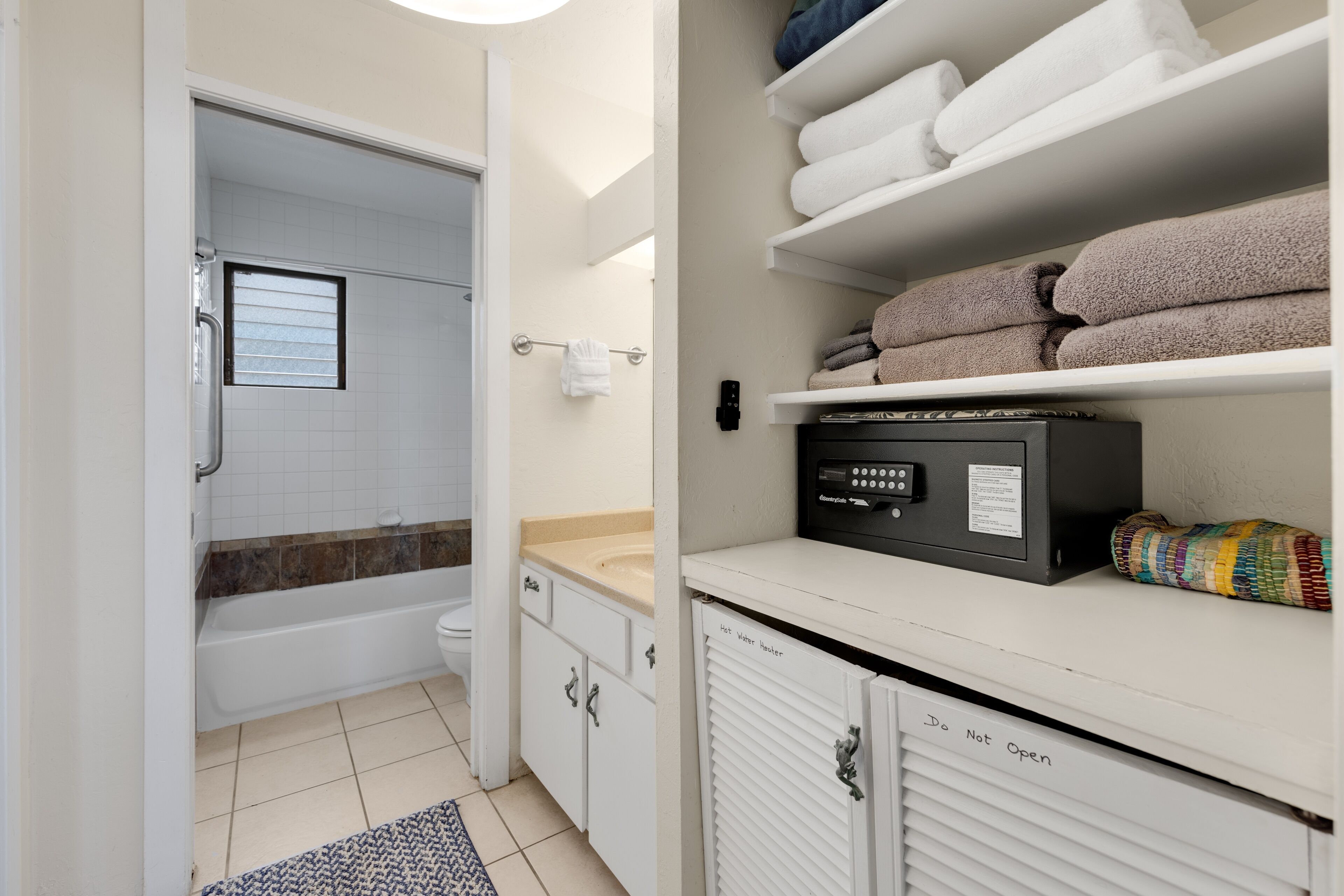 A bathroom with a bathtub, toilet, and a towel rack. There is a shelf with folded towels and a heater.