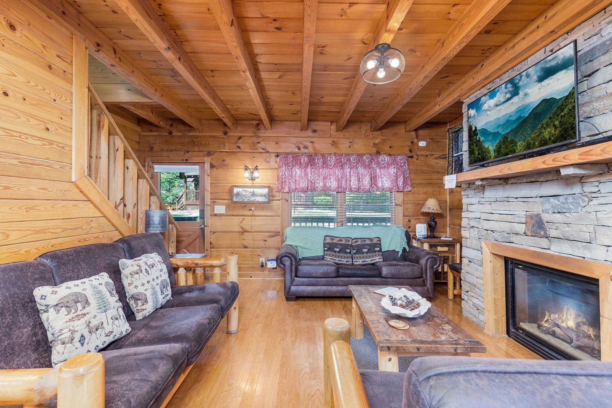 A cozy cabin interior with wooden walls, a fireplace, a sofa, and a television.