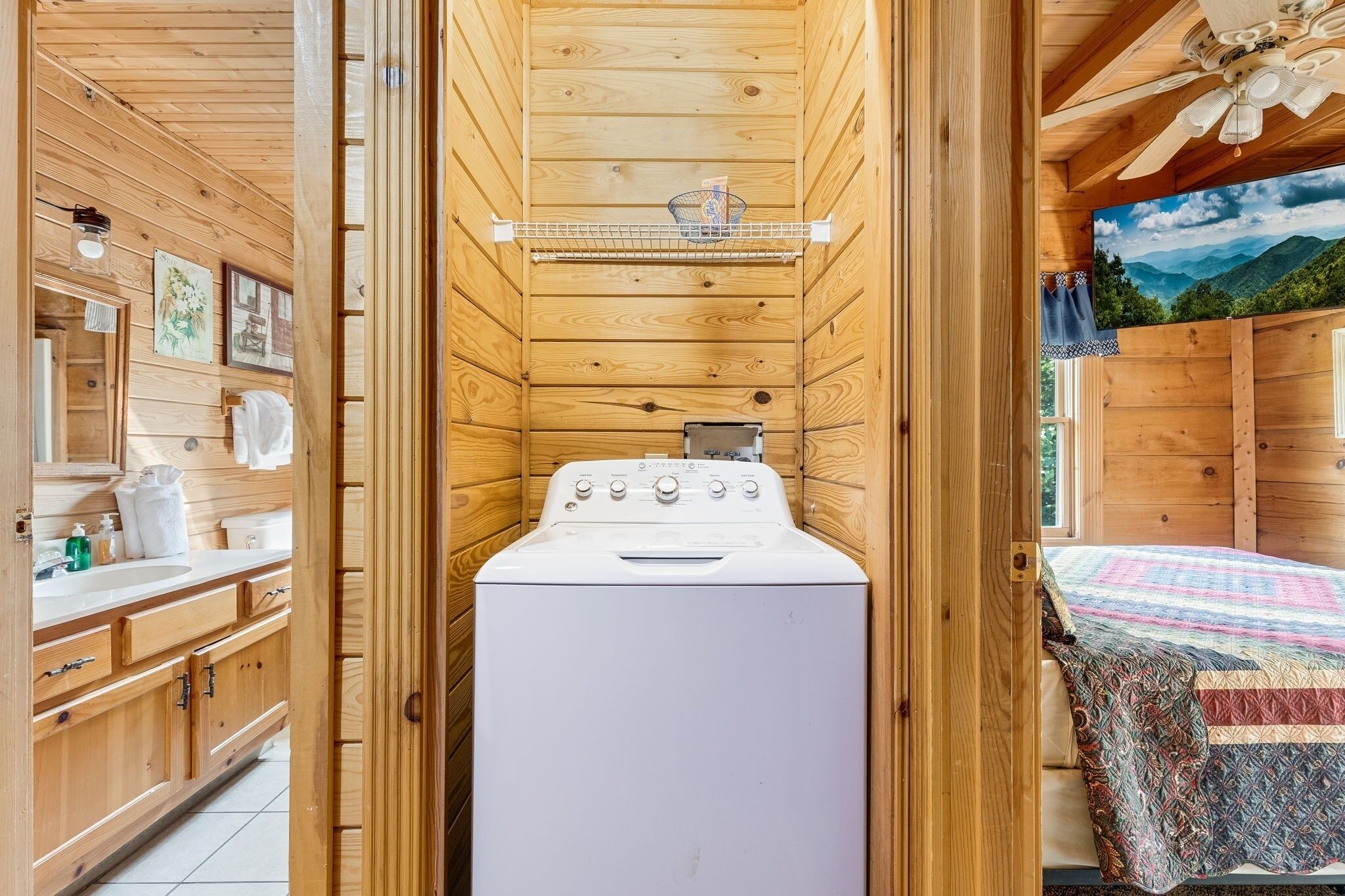 A wooden cabin interior with a washing machine, wooden cabinets, and a bed with a quilt.