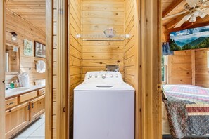 A wooden cabin interior with a washing machine, wooden cabinets, and a bed with a quilt. - Er81 - Family Making Memories 3 Bedroom Cabin by RedAwning (Pigeon Forge)