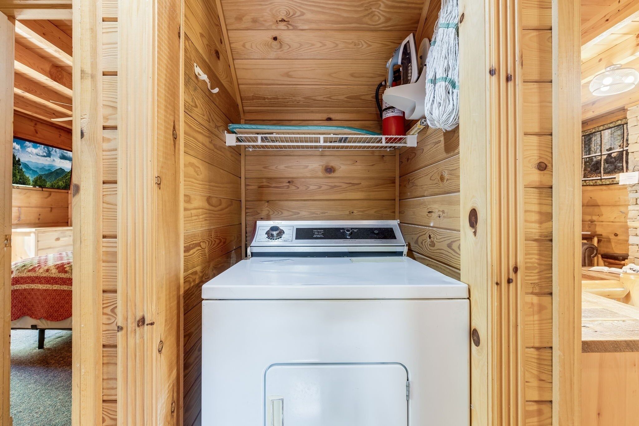 Une petite buanderie avec un lave-linge et un sèche-linge blancs, des murs en bois et une étagère sur laquelle se trouve un récipient rouge.
