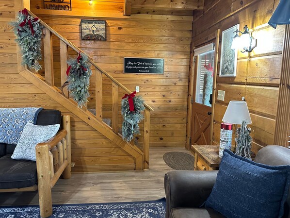 Interior acogedor de una cabaña con escalera de madera, sofá, mesa y decoración navideña.