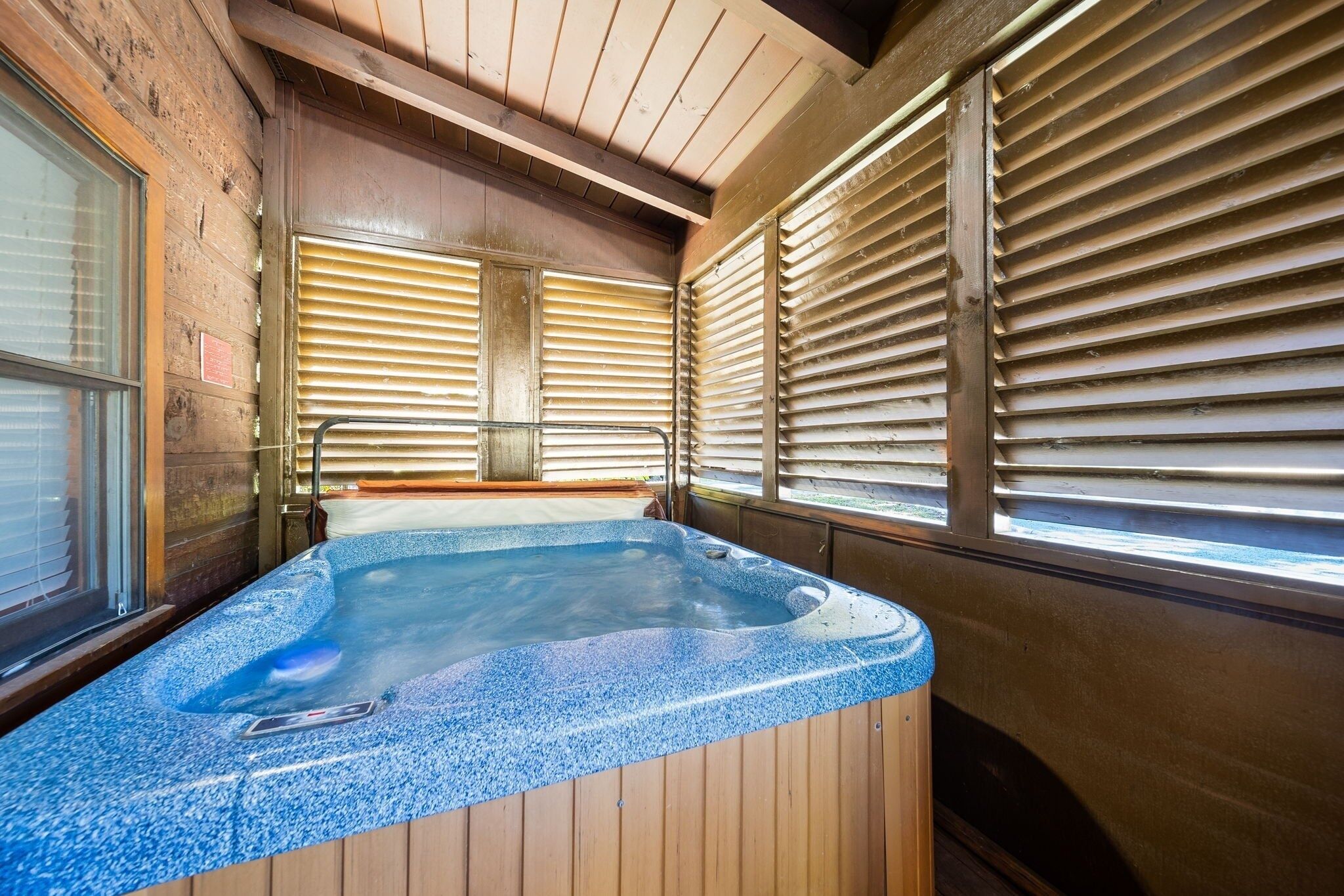 A hot tub with wooden walls and windows with blinds.