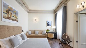 A hotel room with a large bed, a sofa, a desk with a lamp, and a chair. There is a painting on the wall and a door to the right. - Residenza Mondragone  (Florence)