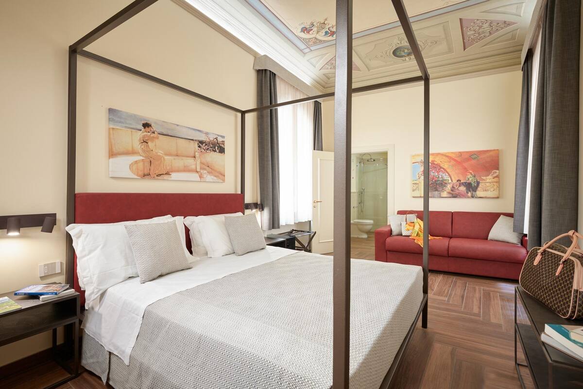 A hotel room with a four-poster bed, a red sofa, and artwork on the walls.