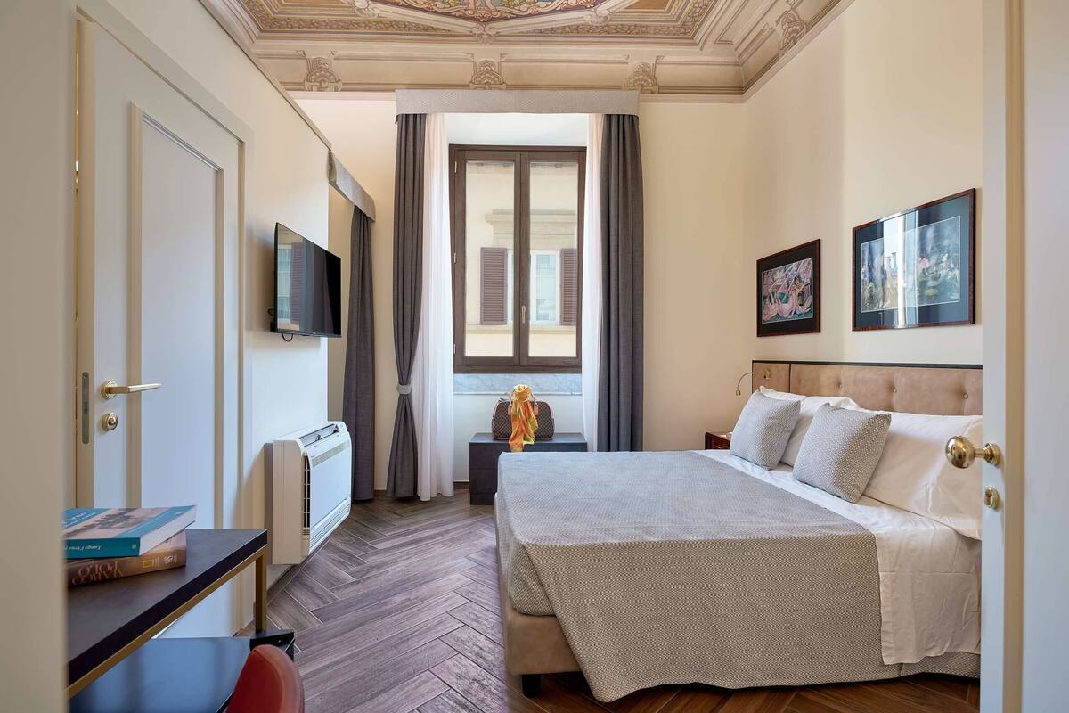A hotel room with a bed, a desk, a TV, and a window with curtains.