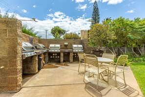 An outdoor barbecue area with stone walls, multiple grills, and a table with chairs. - Maalaea Surf, #g-1 2 Bedroom Condo by RedAwning (Kihei)