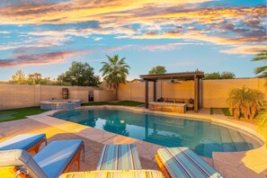 A swimming pool with lounge chairs, a hot tub, and a pergola.