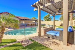 A backyard with a swimming pool, outdoor furniture, and a pergola.