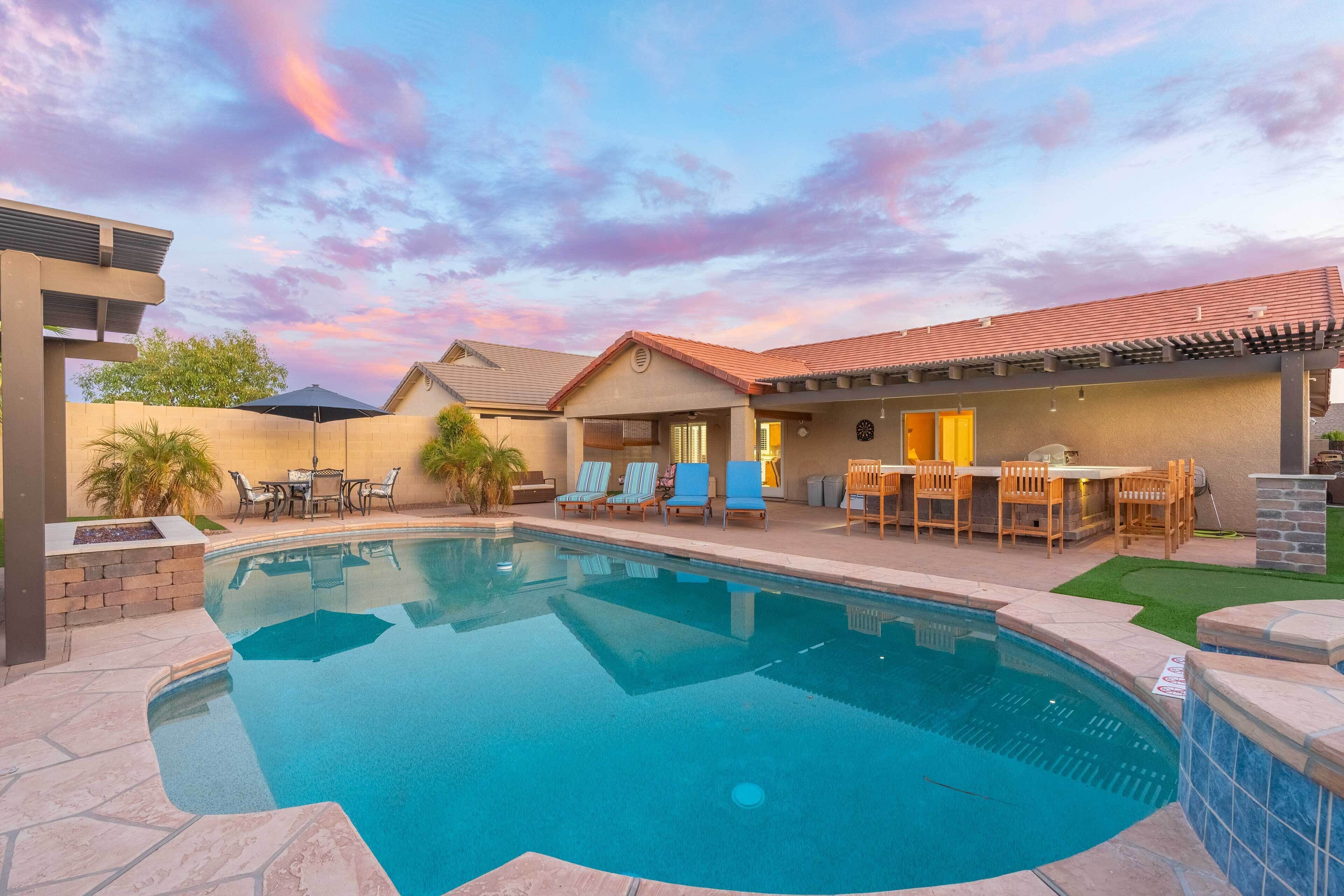 A swimming pool with a patio area, outdoor seating, and a covered section with a bar.