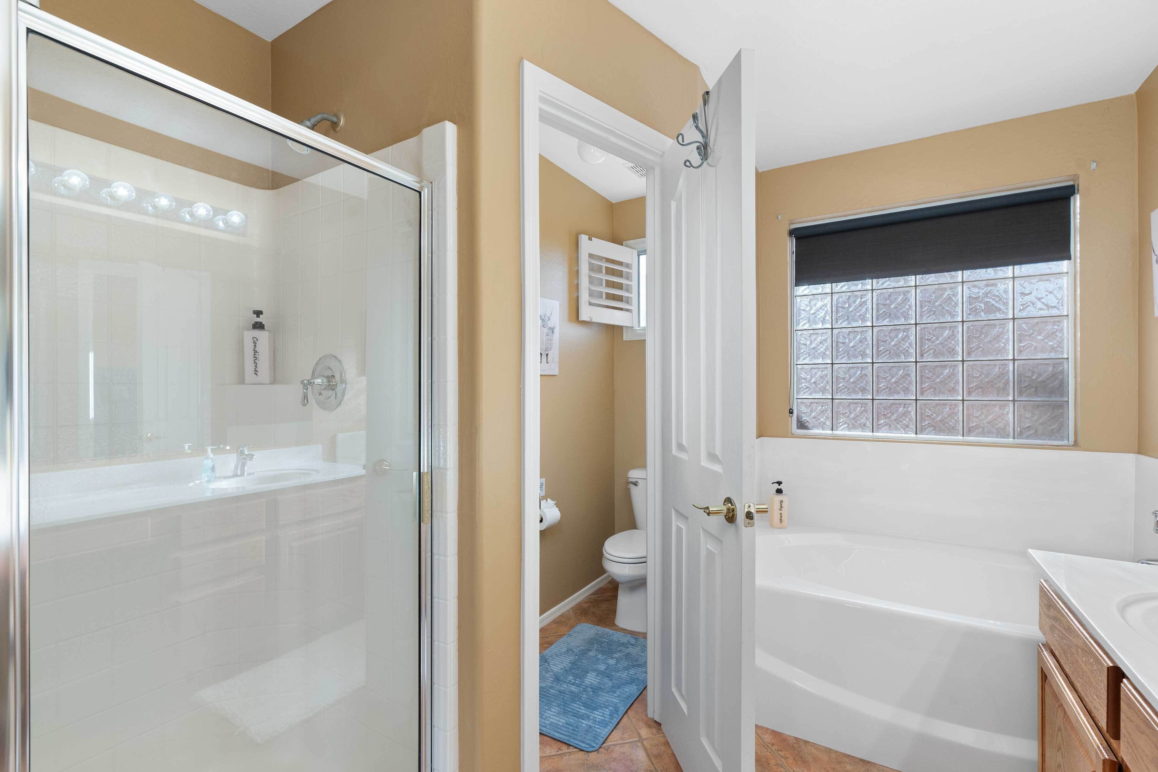 A bathroom with a glass shower enclosure, a white bathtub, and a window with a view.