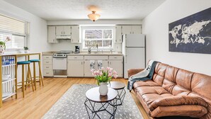 Una cocina moderna con armarios blancos, una zona de comedor con taburetes y un sofá de cuero.