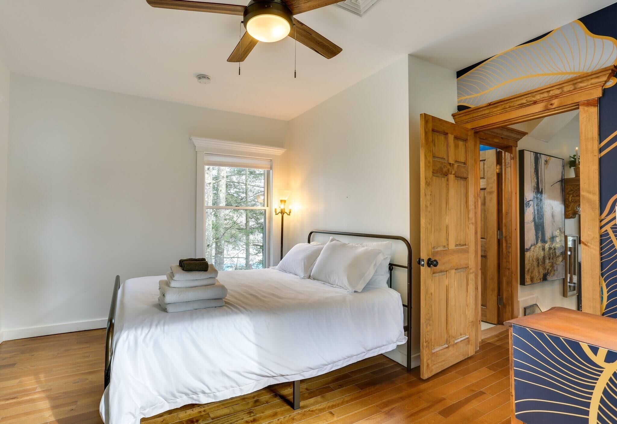 A bedroom with a bed, wooden floor, a ceiling fan, a window, and a wardrobe.
