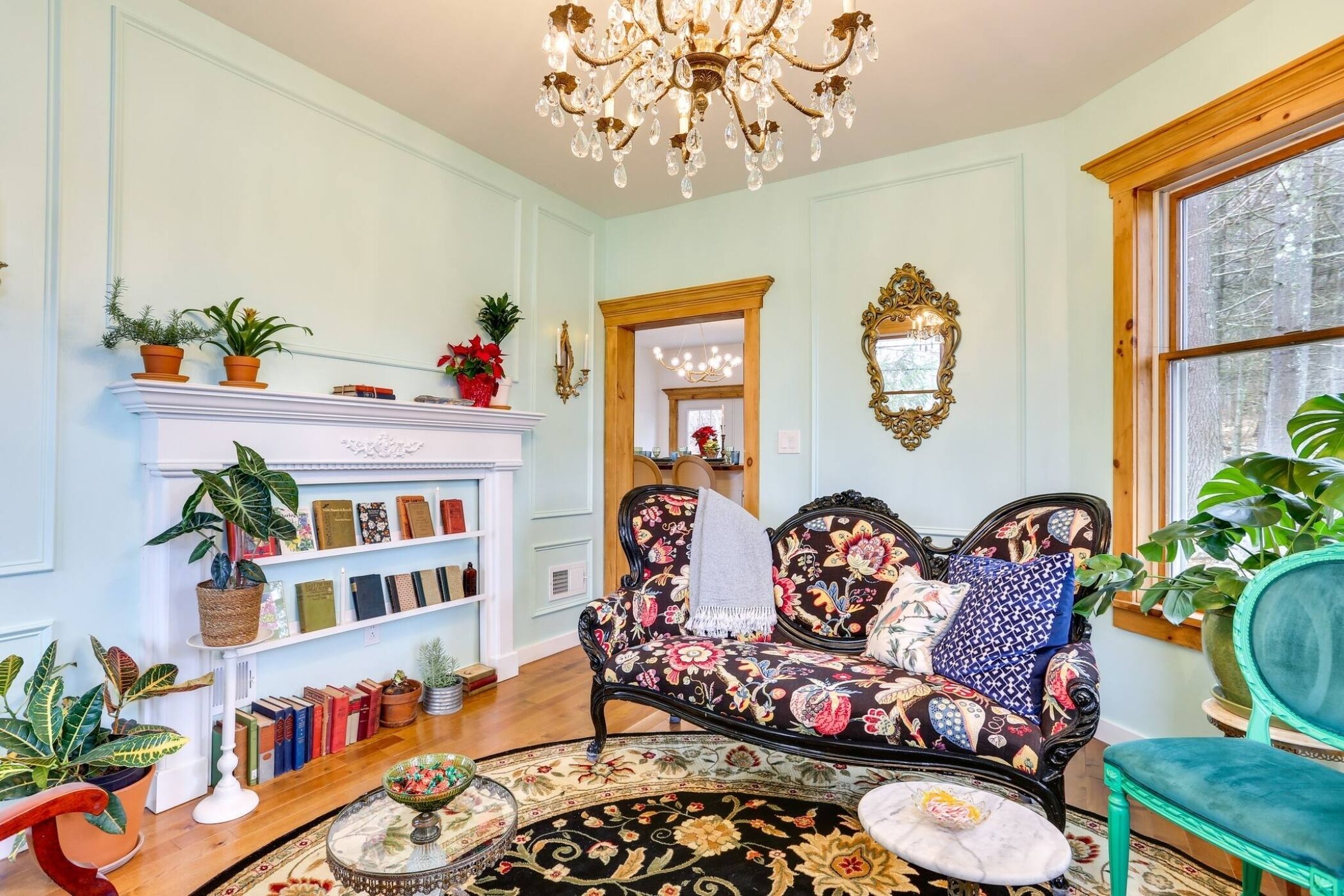 A cozy living room with a fireplace, bookshelves, a floral sofa, and a chandelier.