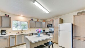 Une cuisine moderne avec des meubles de couleur bois clair, un îlot central doté de tabourets, un réfrigérateur, un four à micro-ondes et une machine à café.