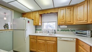 Una cocina compacta con armarios de madera, un refrigerador, un lavavajillas, un tostador y una ventana con persianas.