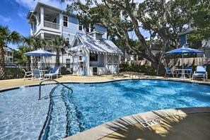 Ein Pool mit Liegestühlen und Sonnenschirmen, umgeben von einem Holenzaun und Bäumen.