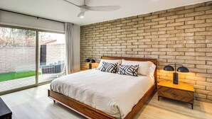Quarto com parede de tijolos, uma cama grande, ventilador de teto e mesa de cabeceira com luminárias.