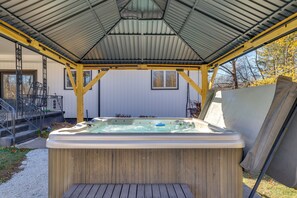A hot tub under a covered patio with a wooden deck, metal roof, and a house in the background. - Game Room & Hot Tub! Cresco Family Home (Mountainhome)