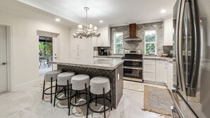 A modern kitchen with a large island, bar stools, stainless steel appliances, and a chandelier. - Pool & Home Theater: Lighthouse Point Home! (Pompano Beach)