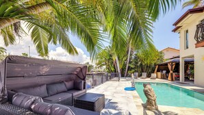 A poolside area with a covered seating area, a stone sculpture, and a clear blue pool. - Pool & Home Theater: Lighthouse Point Home! (Pompano Beach)