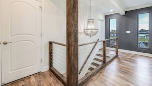 A staircase with wooden railings and a chandelier, leading to a room with large windows and a view of the outdoors. - Pool & Home Theater: Lighthouse Point Home! (Pompano Beach)