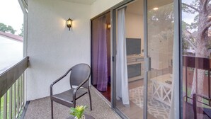 A balcony with a wicker chair, a small table with a plant, and a sliding glass door leading to an outdoor area with a table and chairs. - Chic Montgomery Condo w/ Balcony + Pool Access! (Montgomery)