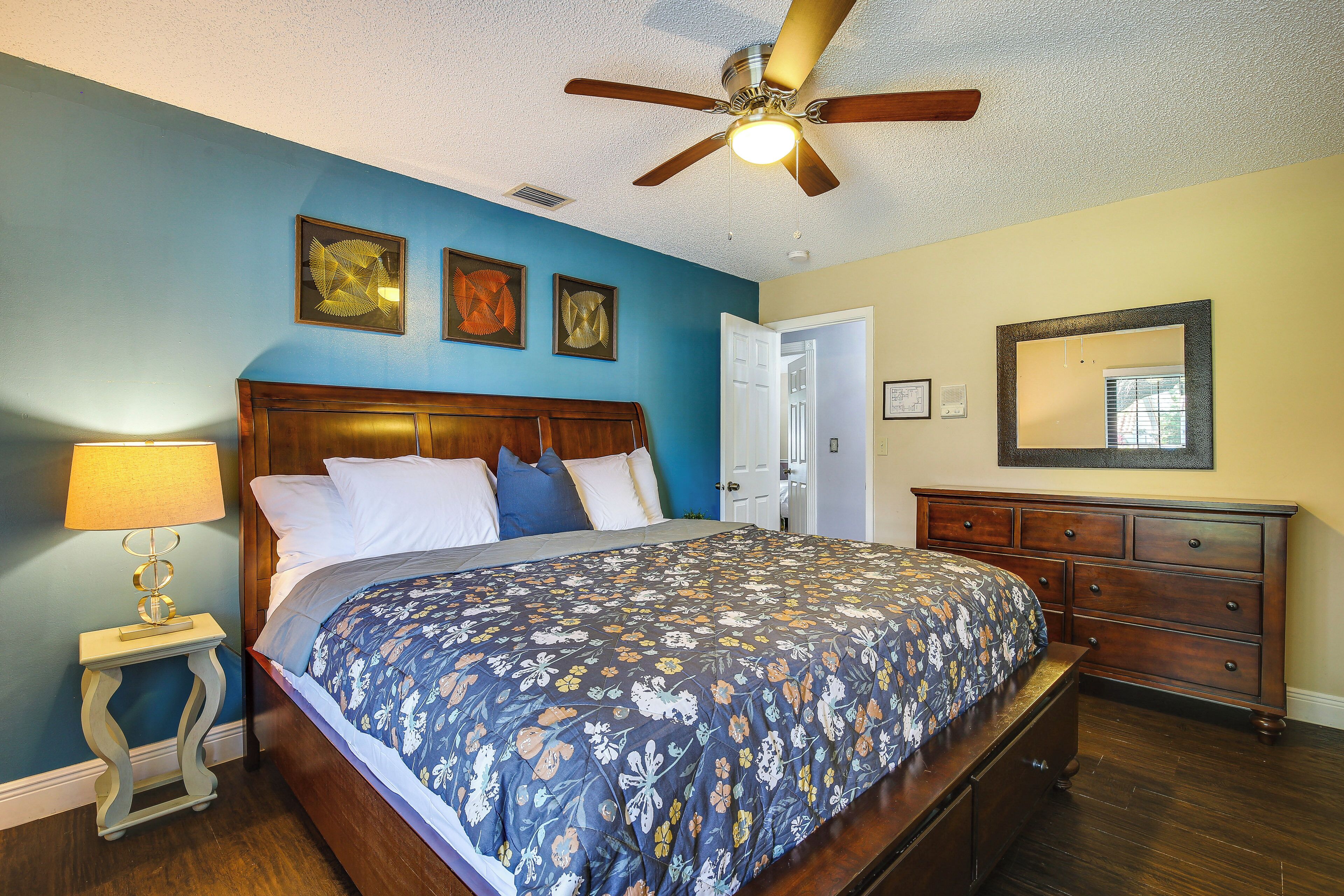 A bedroom with a wooden bed, a nightstand with a lamp, a ceiling fan, and a dresser.