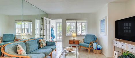 A living room with wicker furniture, a glass coffee table, and a television on a wooden stand.