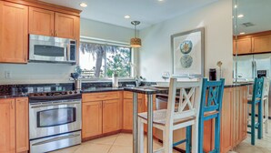 A kitchen with wooden cabinets, stainless steel appliances, a large window, and a dining area with chairs. - Siesta Keys Home w/ Deck Half Mile to Turtle Beach (Siesta Key)