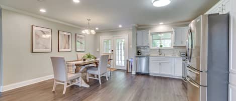 A spacious kitchen with white cabinets, a stainless steel refrigerator, and a dining area with a wooden table and chairs.