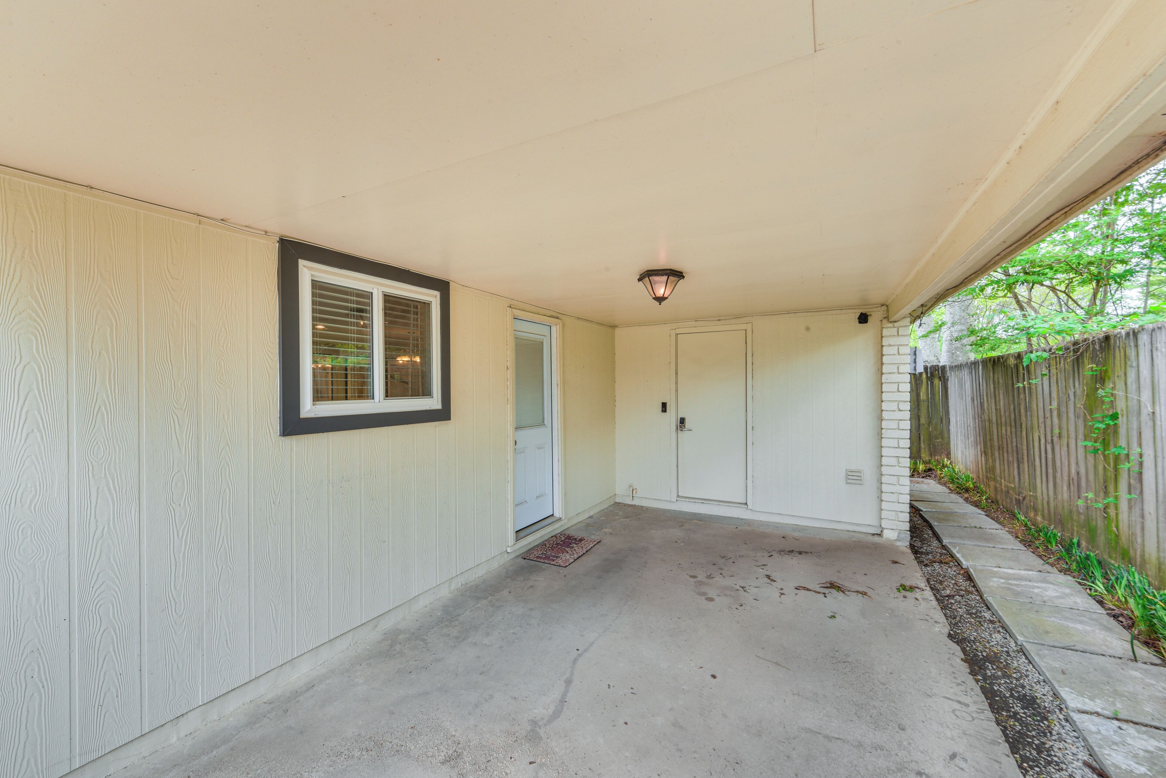 A covered porch with a concrete floor, a door, and a small window with blinds.