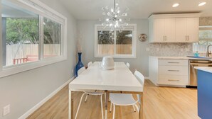 A modern kitchen with a white table, white chairs, a chandelier, and a view of the outdoors. - Boise Retreat ~ 2 Mi to Boise State University! (Boise)