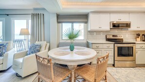 Une cuisine moderne avec des meubles blancs, des appareils en acier inoxydable et une table de salle à manger ronde entourée de chaises en osier.