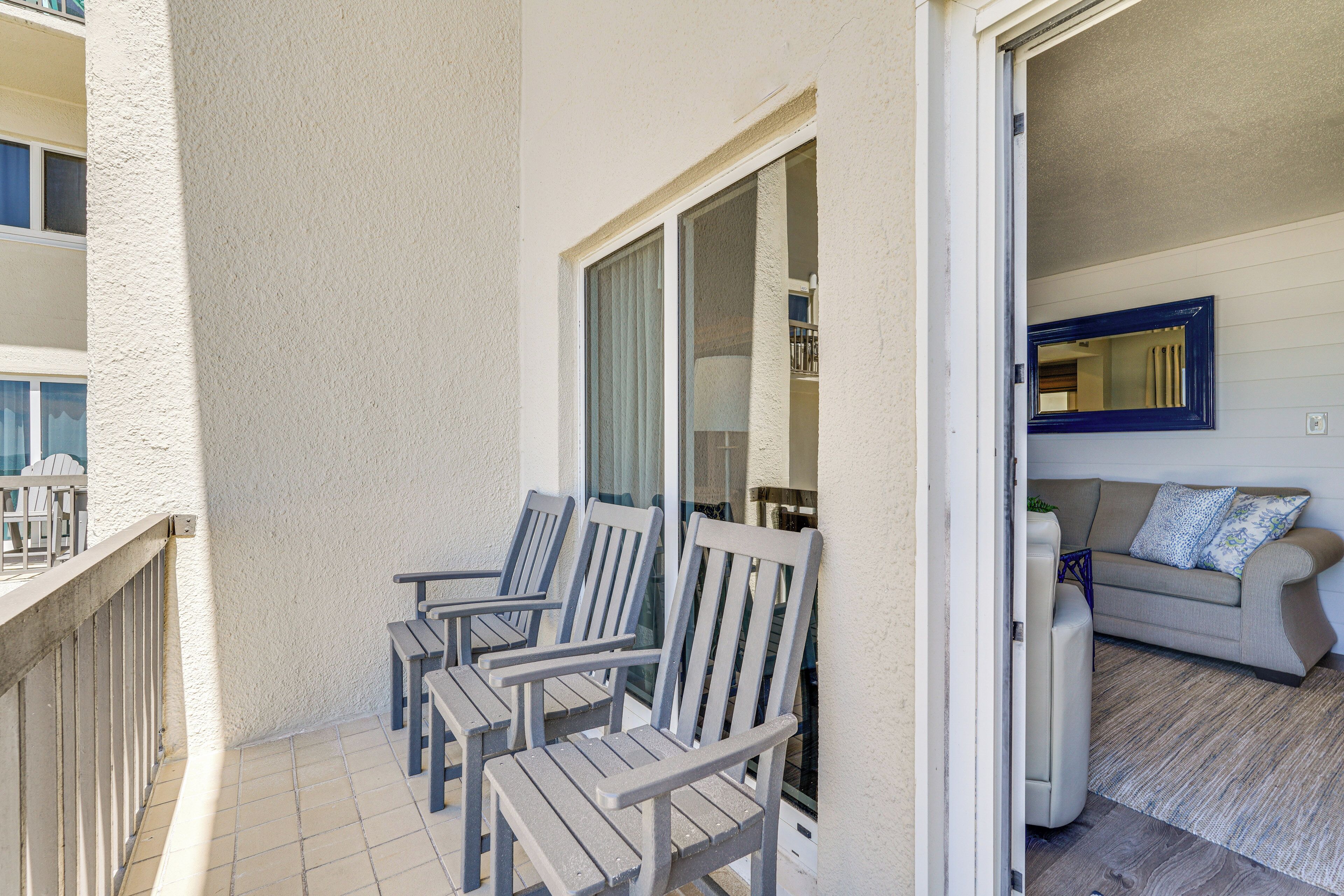 A balcony with two wooden chairs and a glass door leading to an interior room with a sofa and a mirror.