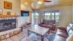 A spacious living room with a stone fireplace, leather sofas, a coffee table, and a ceiling fan. - Near Lakes & Trails: Pet-friendly Cabin in Arizona (Overgaard)