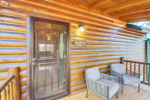 Una baita di legno con una porta in legno, un cartello di benvenuto e due poltrone in vimini su un portico.