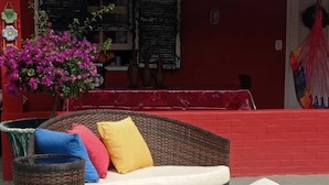 A wicker sofa with cushions in front of a red building with a tiled roof. - FLATS ARPOADOR DE BÚZIOS (Búzios)