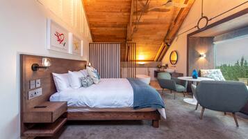 A modern bedroom with a wooden ceiling, a bed with white bedding, a bedside table, a chair, and a small table with a lamp.
