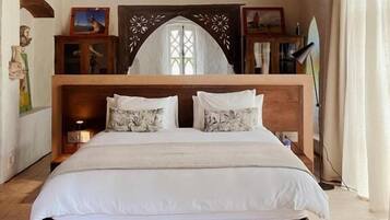 Une chambre avec un plafond en bois, un grand lit avec une literie blanche, une petite fenêtre et une tête de lit décorative en bois.