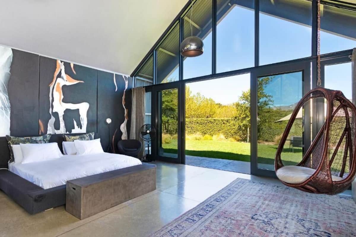 A modern bedroom with a large bed, a hanging chair, and a view of the outdoors.